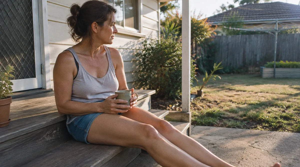 Australian woman sitting on a back step in late afternoon sun with bare legs relaxed, the everyday comfort behind caring for dry skin on legs