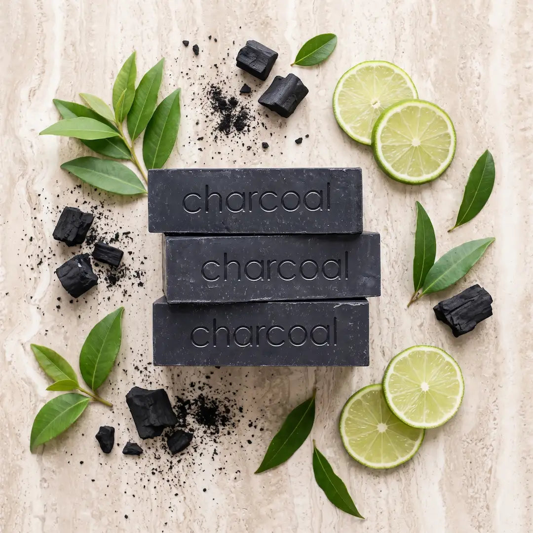 Luxury flatlay of Tasic Pure Oils Activated Charcoal Soap bars styled with activated charcoal chunks, lime and lemon myrtle leaves, and a sliced lime