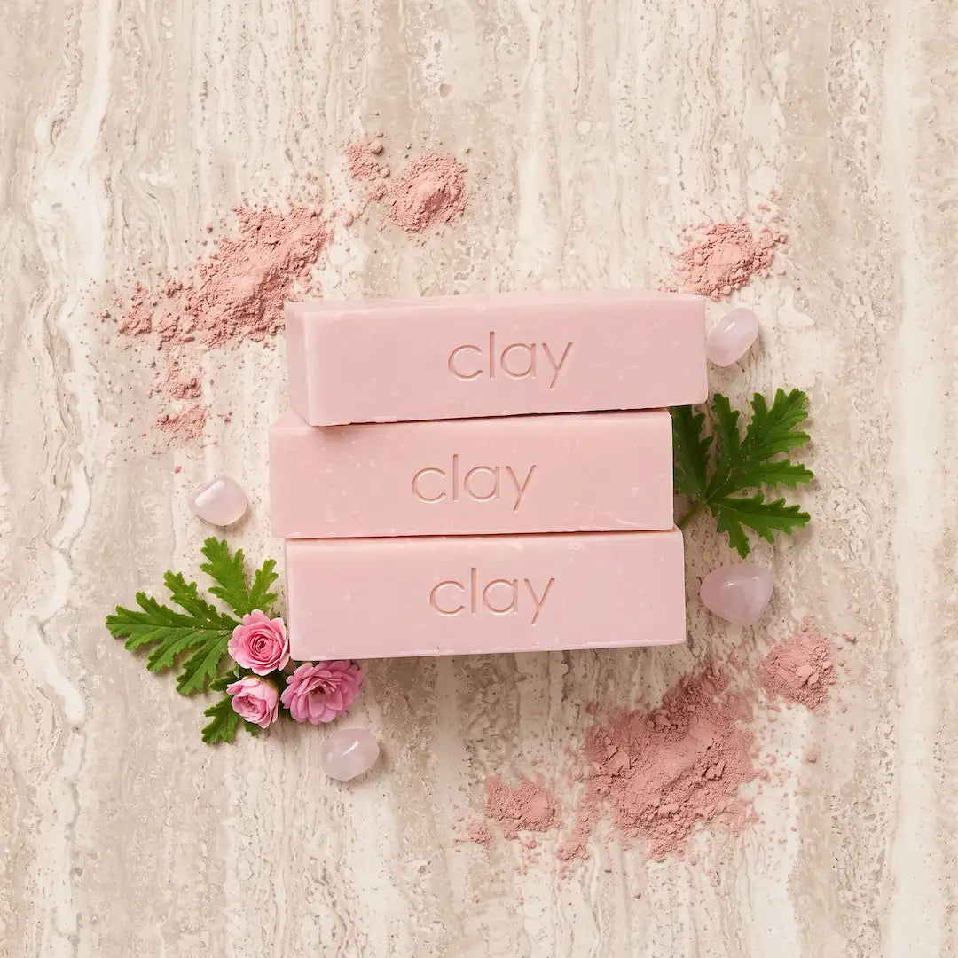 Luxury flatlay of Tasic Pure Oils Australian Pink Clay Soap bars styled with raw pink clay powder and rose geranium sprigs