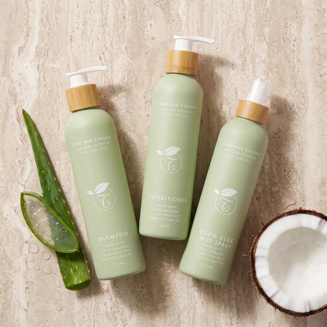 Luxury flatlay of the Tasic Pure Oils Long and Strong shampoo, conditioner, and Coco Aloe Mist trio styled with sliced aloe vera and cracked coconut