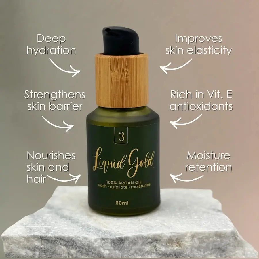 Bottle of 'Liquid Gold' argan oil with text highlighting its benefits on a marble surface.