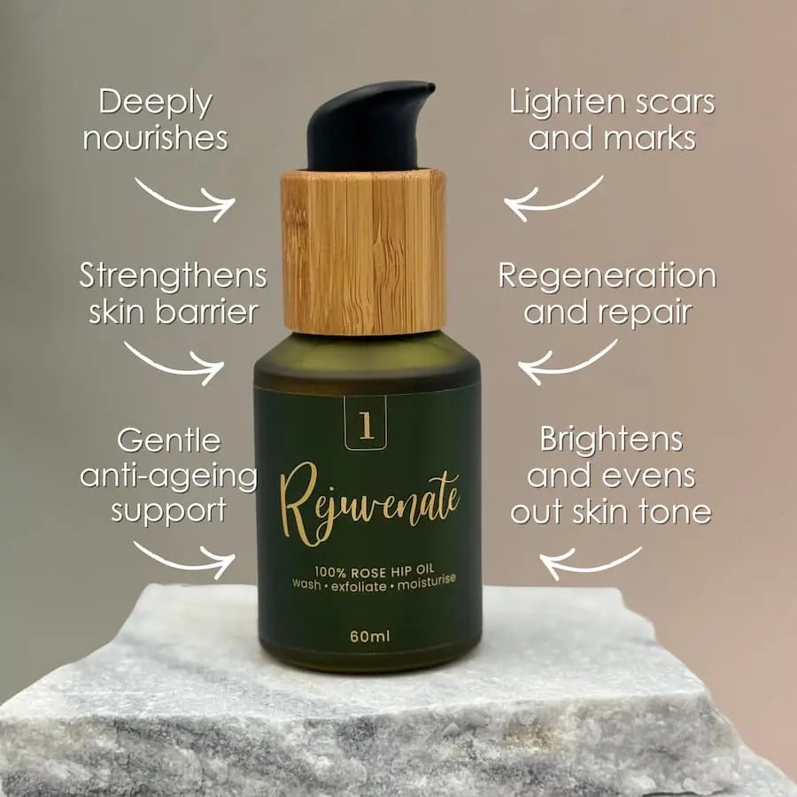 Bottle of Rejuvenate rose hip oil with text highlighting its benefits on a marble surface.