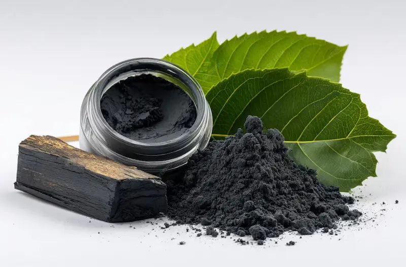 Black powder in a jar with a wooden block and green leaves on a light background