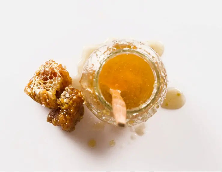 Jar of honey with honeycomb pieces on a white background