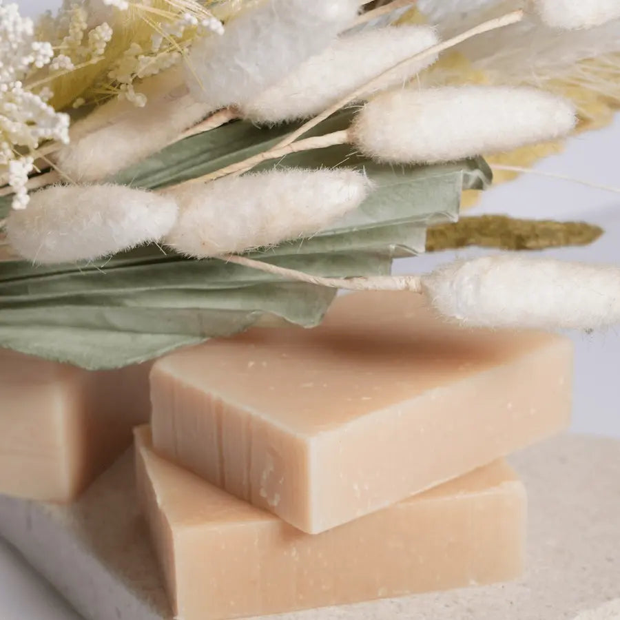 Three bars of soap with a natural background featuring cotton and greenery.