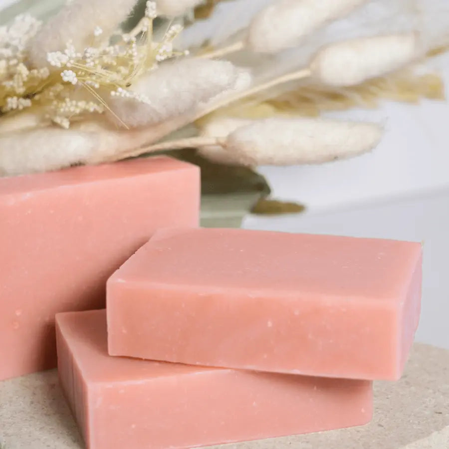 Three pink soap bars on a textured surface with a blurred natural background