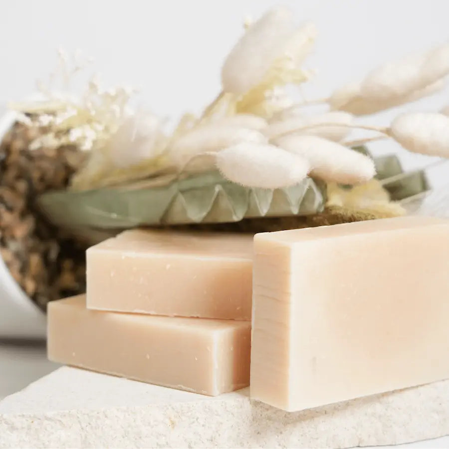 Three bars of soap on a white surface with dried flowers in the background