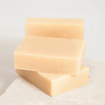 Three bars of soap stacked on a textured surface with a light background